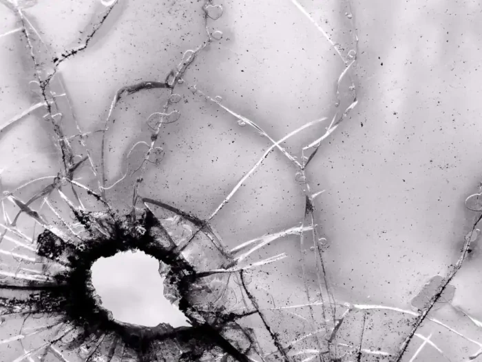 A bullet hole blackens the lower left-hand corner of a window in this black and white picture and the clear glass is cracking as a result.